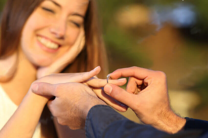 Freund schiebt einen Verlobungsring in Weißgold auf den Ringfinger der Freundin